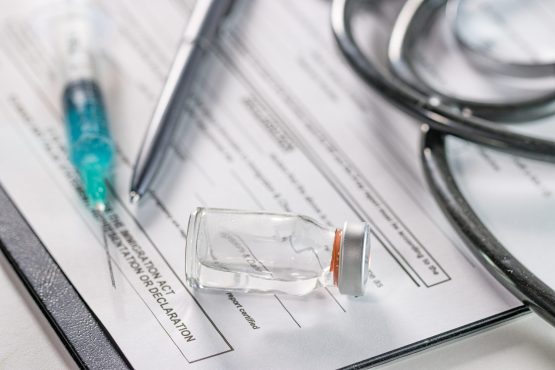 A closeup of an ampoule and a needle syringe on a document with a phonendoscope on the background
